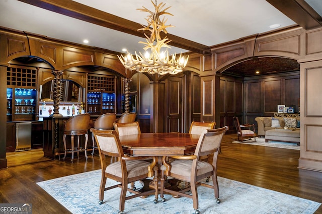 dining space with wood walls, an inviting chandelier, bar area, dark hardwood / wood-style floors, and beam ceiling