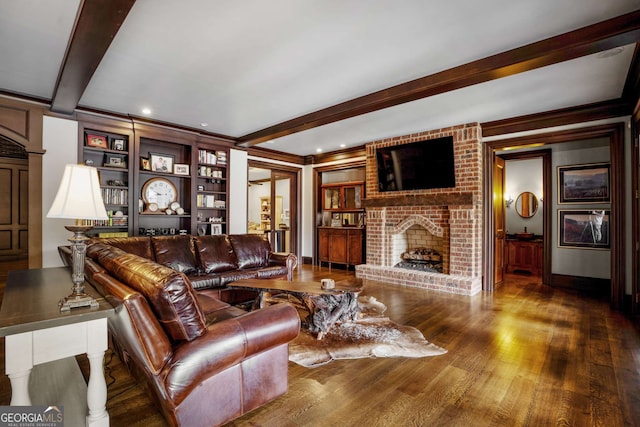 living room with beam ceiling, built in shelves, a brick fireplace, crown molding, and wood-type flooring