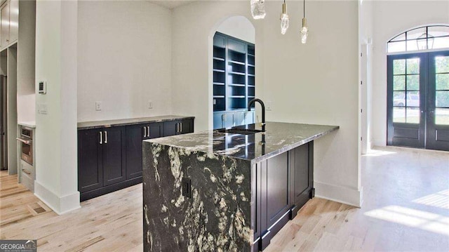 bar featuring dark stone countertops, pendant lighting, french doors, sink, and light hardwood / wood-style flooring