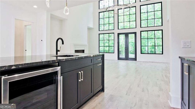 kitchen featuring dark stone countertops, wine cooler, hanging light fixtures, french doors, and sink