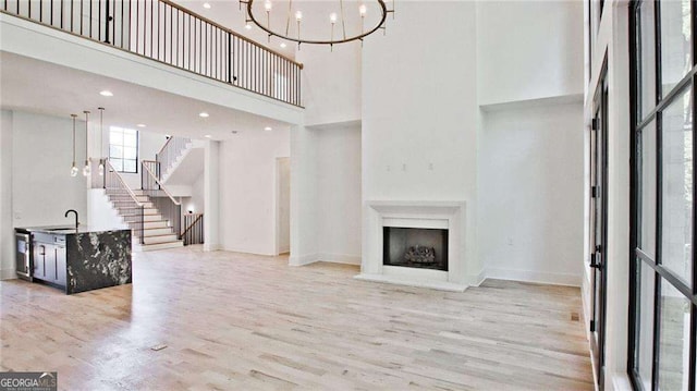 living room with sink, an inviting chandelier, a high ceiling, and light wood-type flooring