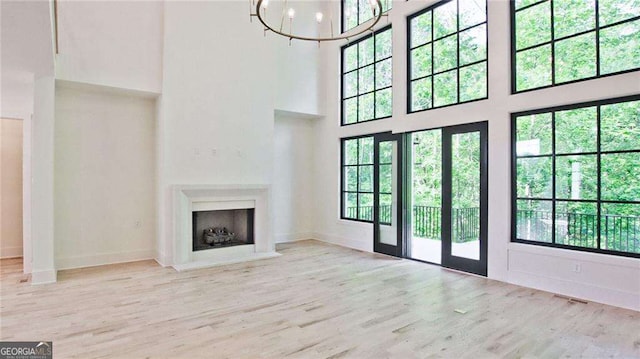 unfurnished living room with a healthy amount of sunlight, light hardwood / wood-style flooring, a towering ceiling, and a chandelier