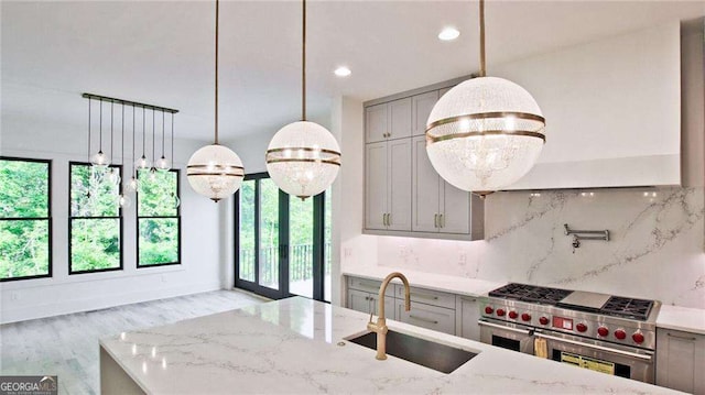 kitchen with range with two ovens, pendant lighting, light stone counters, sink, and tasteful backsplash