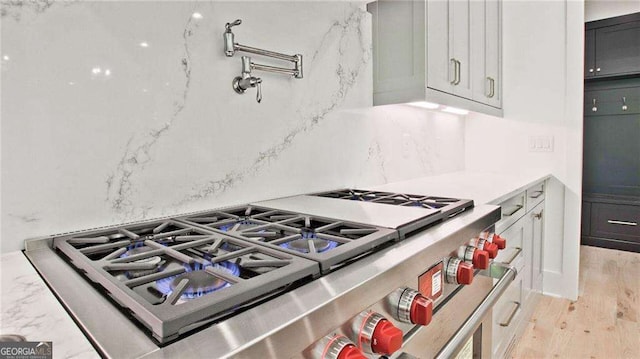 kitchen with light hardwood / wood-style floors, white cabinetry, backsplash, and high end stove