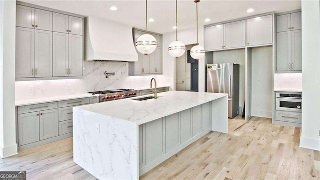 kitchen featuring light stone countertops, sink, stainless steel appliances, a kitchen island with sink, and custom range hood