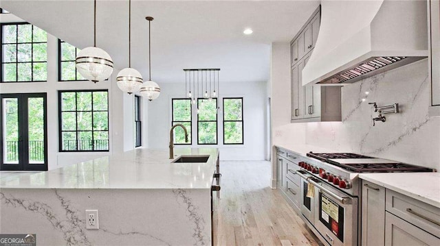 kitchen featuring custom exhaust hood, light stone countertops, range with two ovens, sink, and backsplash