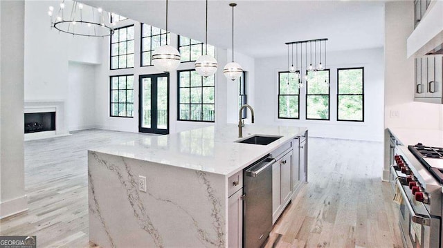 kitchen featuring a kitchen island with sink, appliances with stainless steel finishes, custom range hood, light stone counters, and sink