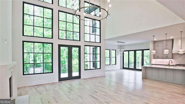 unfurnished living room featuring light hardwood / wood-style flooring, french doors, an inviting chandelier, and a towering ceiling