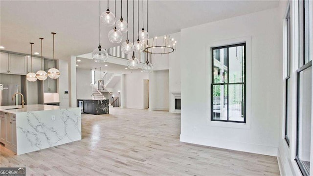 interior space with sink, pendant lighting, a kitchen island with sink, and light stone countertops