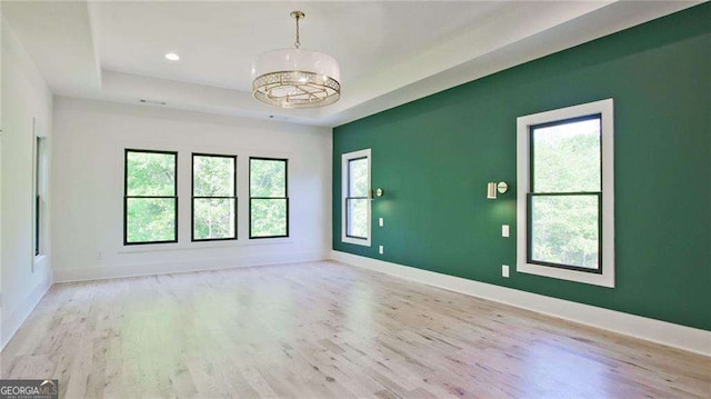 empty room with light wood-type flooring and a tray ceiling