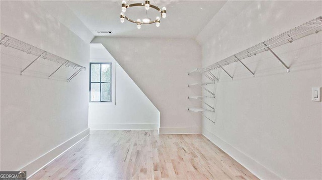 walk in closet with light hardwood / wood-style floors, lofted ceiling, and a notable chandelier