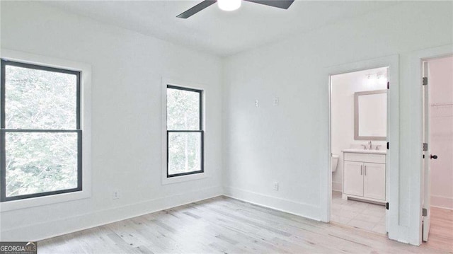 unfurnished bedroom featuring ceiling fan, light wood-type flooring, connected bathroom, and multiple windows