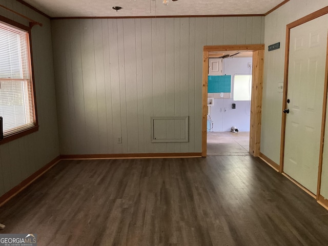 empty room featuring ceiling fan, dark hardwood / wood-style flooring, crown molding, and wood walls