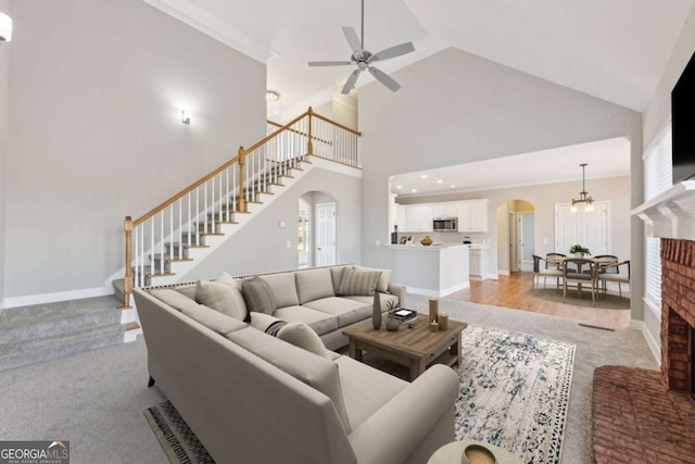 carpeted living room featuring crown molding, a brick fireplace, high vaulted ceiling, and ceiling fan with notable chandelier