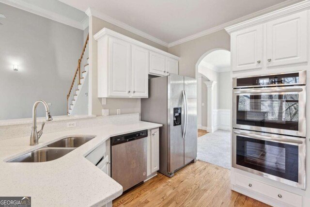 kitchen with appliances with stainless steel finishes, light wood-type flooring, crown molding, white cabinets, and sink