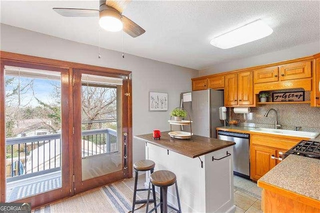 kitchen featuring appliances with stainless steel finishes, a center island, wood counters, ceiling fan, and sink