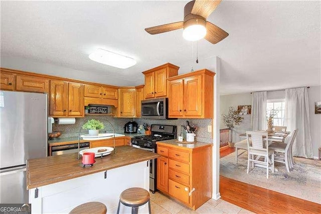 kitchen with stainless steel appliances, butcher block counters, ceiling fan, light tile patterned floors, and decorative backsplash