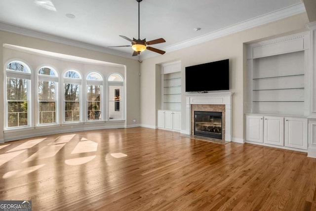 unfurnished living room with a premium fireplace, ornamental molding, light wood-type flooring, and built in features