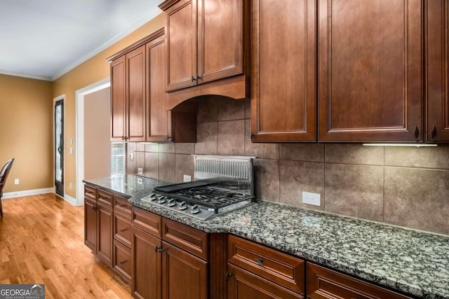 kitchen with dark stone counters, light hardwood / wood-style flooring, stainless steel gas cooktop, and crown molding