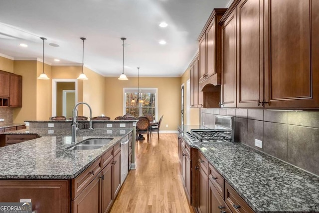 kitchen with sink, pendant lighting, dark stone counters, and a center island with sink