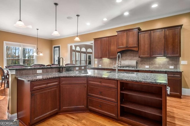 kitchen with decorative light fixtures, a kitchen island with sink, and dark stone countertops