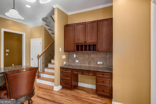 kitchen featuring built in desk, decorative light fixtures, dark stone countertops, light wood-type flooring, and ornamental molding