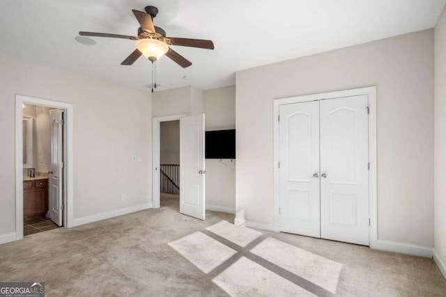 unfurnished bedroom featuring ceiling fan, light colored carpet, a closet, and ensuite bath