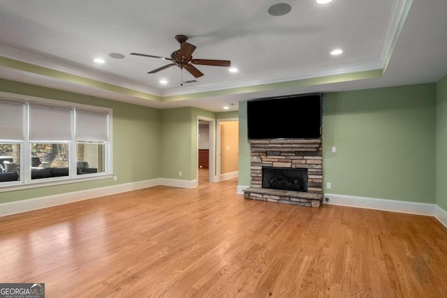 unfurnished living room with a raised ceiling, light wood-type flooring, crown molding, a fireplace, and ceiling fan