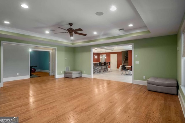 unfurnished living room featuring ceiling fan, light wood-type flooring, a tray ceiling, and ornamental molding