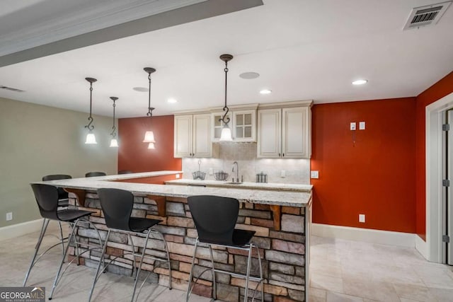 kitchen with cream cabinetry, hanging light fixtures, light stone countertops, sink, and backsplash