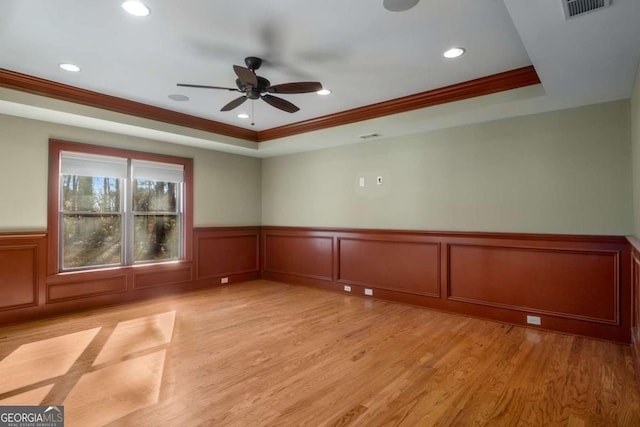 spare room featuring a raised ceiling, ornamental molding, and light hardwood / wood-style floors