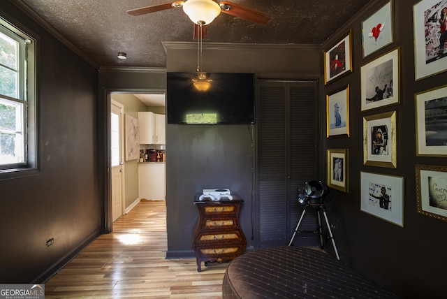 corridor featuring a textured ceiling, ornamental molding, plenty of natural light, and light wood-type flooring