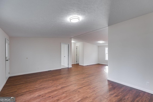 spare room with a textured ceiling, wood finished floors, lofted ceiling, and baseboards