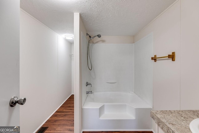 bathroom featuring a textured ceiling, wood finished floors, vanity, visible vents, and tub / shower combination