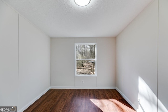 unfurnished room featuring a textured ceiling, dark wood finished floors, and baseboards