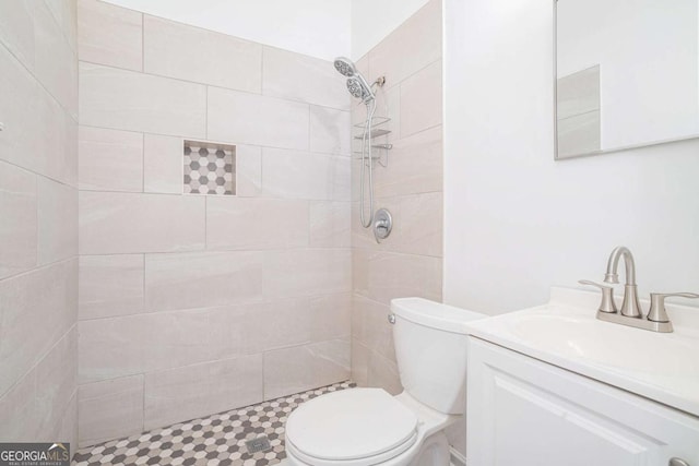 bathroom with toilet, a tile shower, and vanity