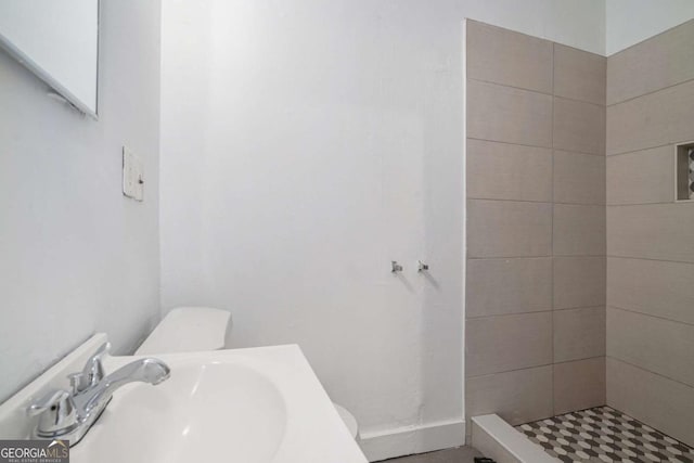 bathroom with sink, a tile shower, and toilet