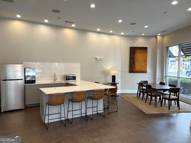 kitchen featuring sink, a breakfast bar area, stainless steel fridge, backsplash, and kitchen peninsula