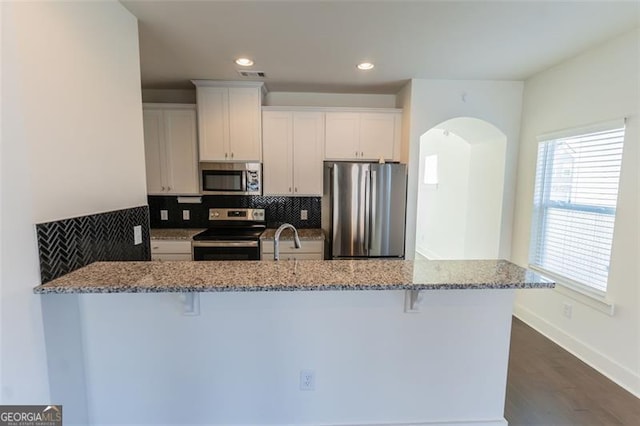 kitchen featuring a kitchen breakfast bar, white cabinetry, light stone counters, and appliances with stainless steel finishes