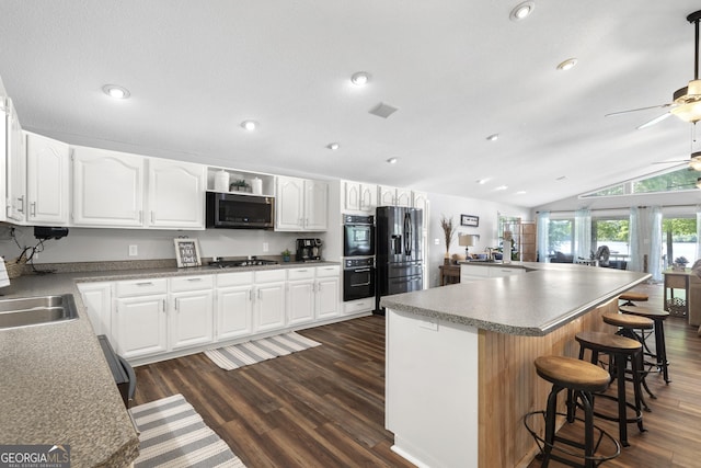 kitchen featuring white cabinets, lofted ceiling, a breakfast bar area, a kitchen island, and black appliances