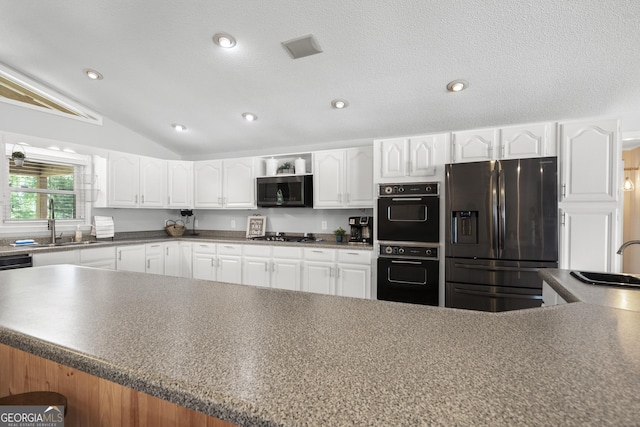 kitchen featuring a textured ceiling, vaulted ceiling, stainless steel appliances, white cabinetry, and sink