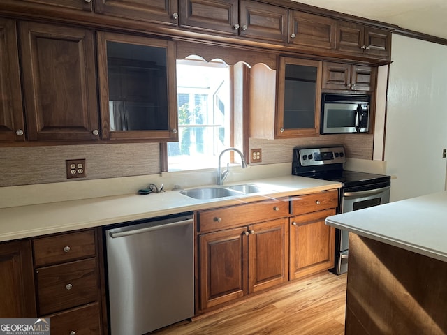 kitchen with stainless steel appliances, ornamental molding, light hardwood / wood-style floors, and sink