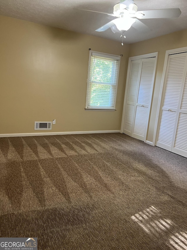 unfurnished bedroom featuring ceiling fan, two closets, a textured ceiling, and carpet flooring