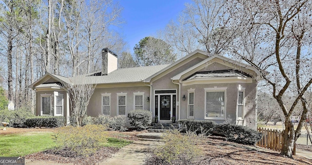 view of front facade with fence, a chimney, and stucco siding