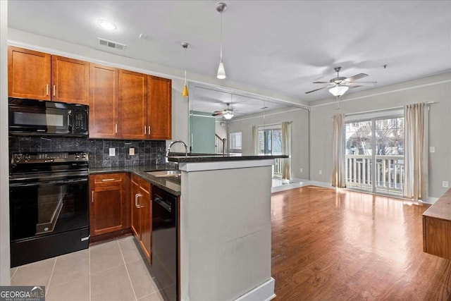 kitchen featuring kitchen peninsula, hanging light fixtures, black appliances, decorative backsplash, and dark stone countertops