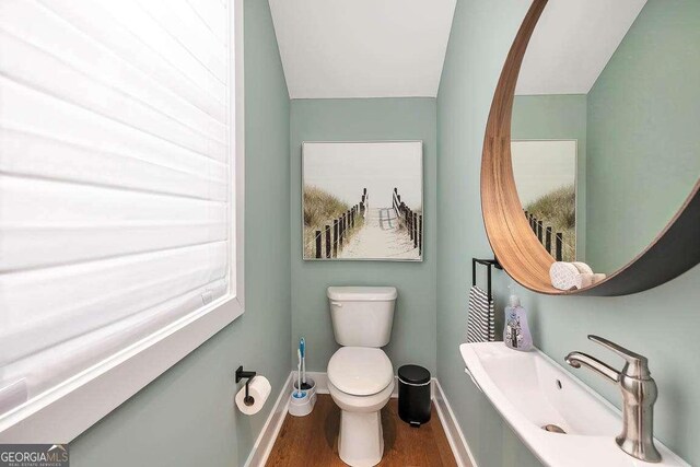 half bath featuring toilet, a sink, wood finished floors, baseboards, and vaulted ceiling