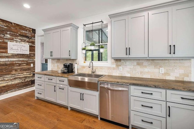 kitchen featuring dishwasher, wood walls, light hardwood / wood-style floors, gray cabinets, and sink