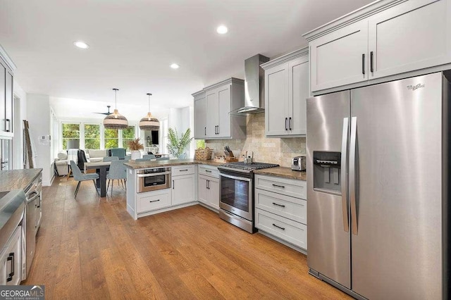 kitchen featuring decorative light fixtures, wall chimney exhaust hood, kitchen peninsula, decorative backsplash, and appliances with stainless steel finishes