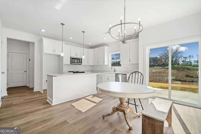 kitchen featuring a wealth of natural light, pendant lighting, stainless steel appliances, a kitchen island, and white cabinetry