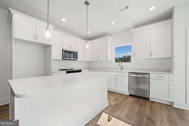 kitchen featuring pendant lighting, a center island, light hardwood / wood-style floors, white cabinets, and appliances with stainless steel finishes